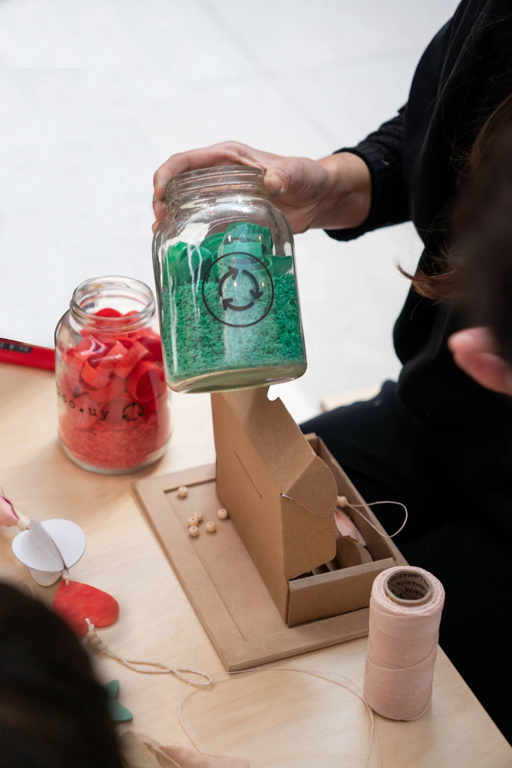 Frasco con material reciclado verde sostenido a mano en un taller creativo de ONÍRICA